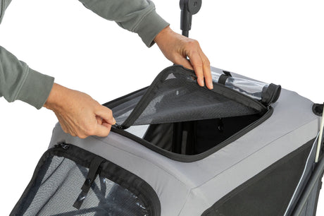 Hände öffnen den Reißverschluss eines grauen Fahrradanhängers mit Netzstoff oben.