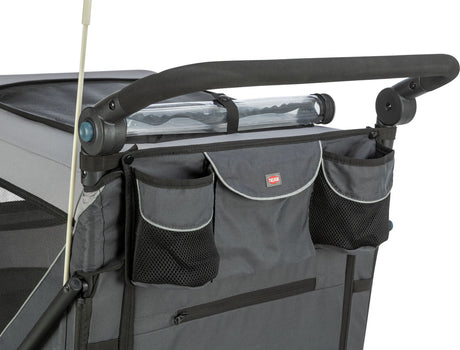 Ein grauer Transportwagen mit schwarzem Griff und mehreren Taschen, teilweise aus Netzmaterial, ist abgebildet.