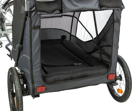 Ein schwarzer Fahrradanhänger mit zwei Rädern und offenem Innenraum, verbunden mit einem Fahrrad, Netzseiten und reflektierenden Rücklichtern.