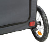 Grauer Fahrradanhänger mit schwarzem Rahmen und Reflektor an Rad und Stoffseite, schwarzer Reifen mit gelbem Reflektor.