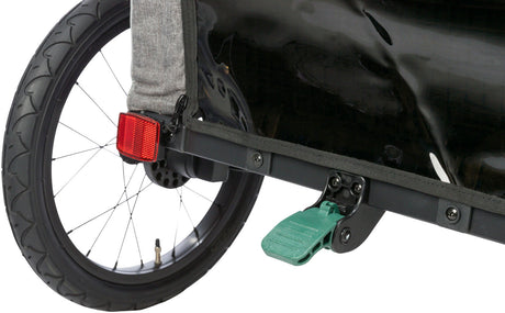 Rad eines Fahrradanhängers mit rotem Reflektor, schwarzem Schutzblech und grünem Pedal auf grauer Stoffbespannung.