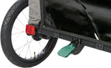 Rad eines Fahrradanhängers mit rotem Reflektor, schwarzem Schutzblech und grünem Pedal auf grauer Stoffbespannung.