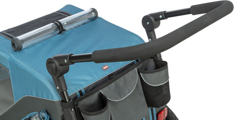 Blauer Fahrradanhänger mit zwei schwarzen Griffen und grauen Taschen, die an der Rückseite befestigt sind.