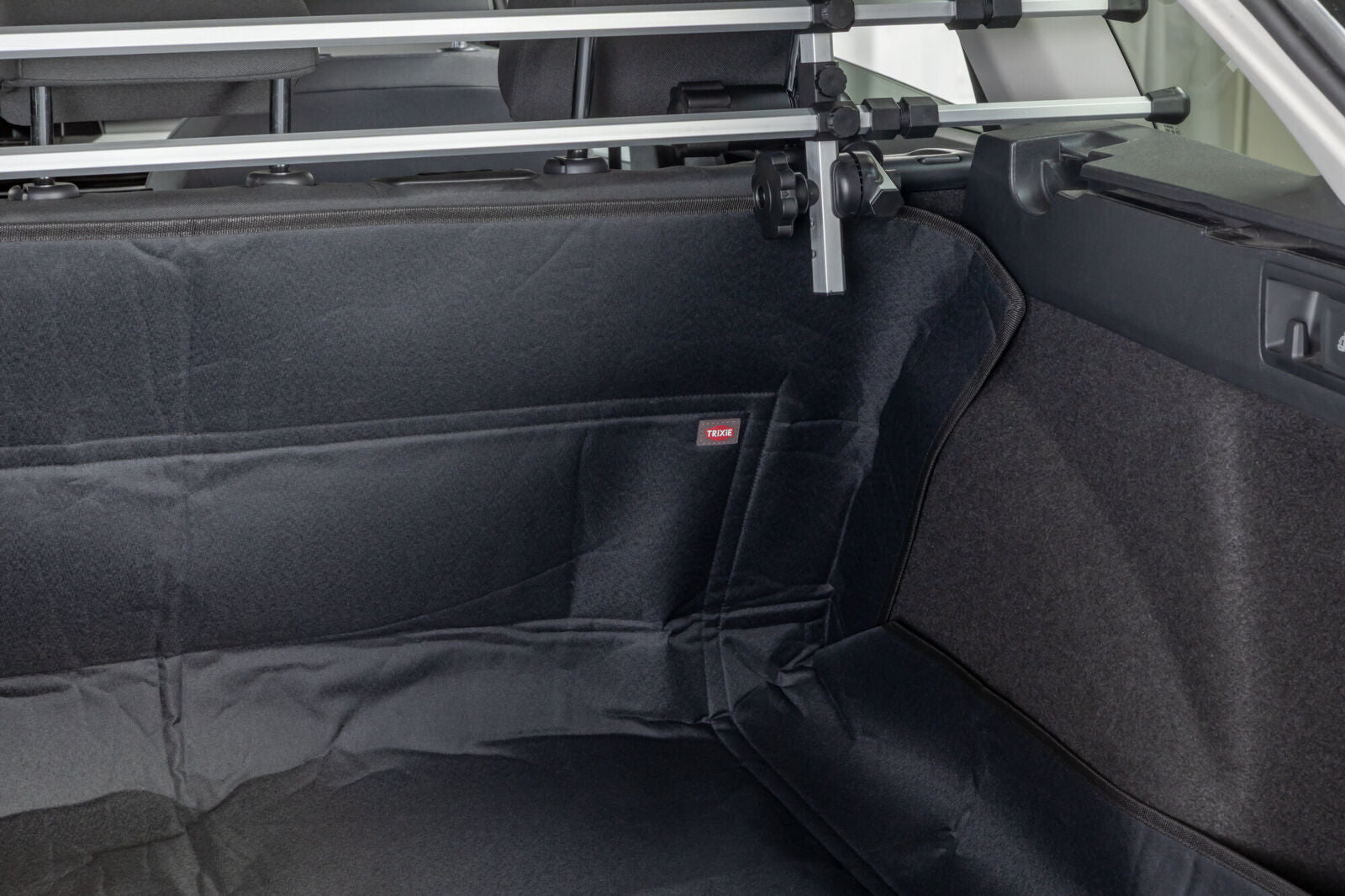 Schwarze Kofferraumauskleidung in einem Auto mit sichtbarem Schutzgitter und einem kleinen roten Etikett.