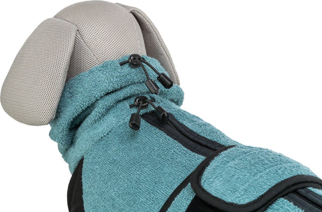 Ein Hundemantel in Türkis mit schwarzen Reißverschlüssen und Kordelzug auf einem Stoffmodell.