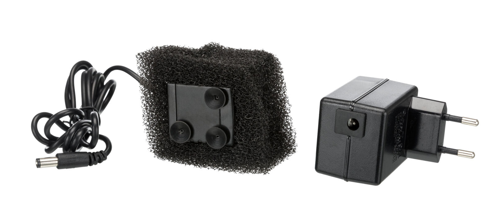 Schwarzes Netzteil mit Eurostecker und Kabel, daneben schwarzer rechteckiger Schwamm mit Saugnäpfen.