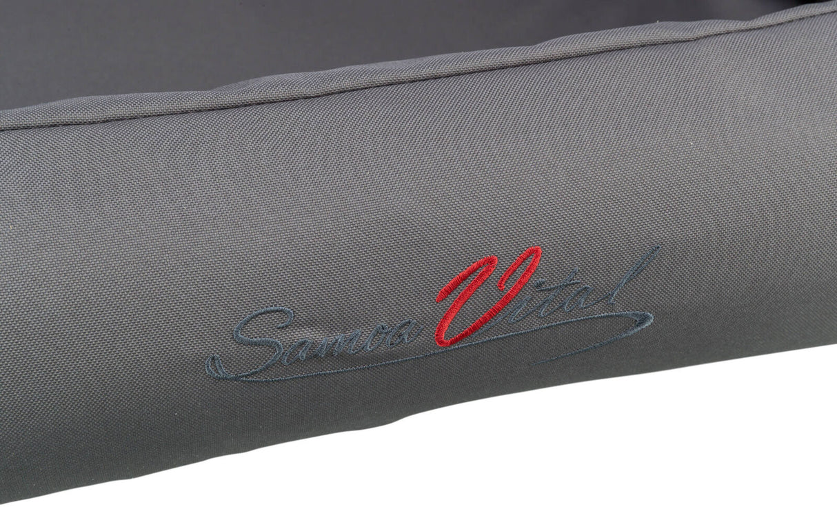 Graues Textil mit aufgestickter Schrift in Rot und Blau, teilweise lesbar als "Samoa Vital".