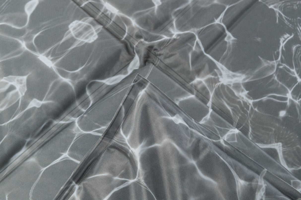 Graues gefaltetes Material mit weißen, fließenden Linien, die an Lichtreflexionen auf Wasser erinnern.