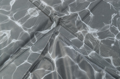 Graues gefaltetes Material mit weißen, fließenden Linien, die an Lichtreflexionen auf Wasser erinnern.