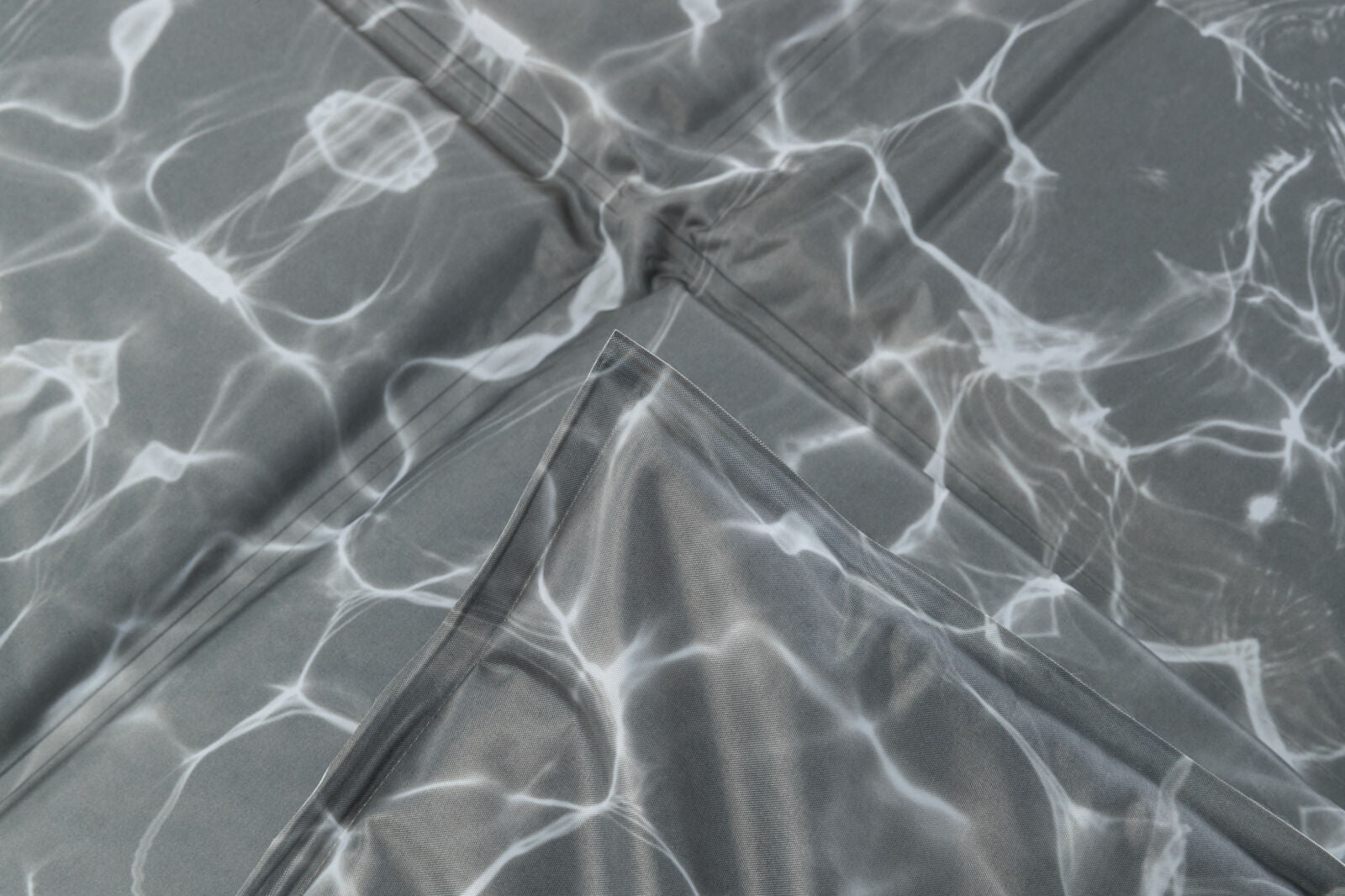Graues gefaltetes Material mit weißen, fließenden Linien, die an Lichtreflexionen auf Wasser erinnern.
