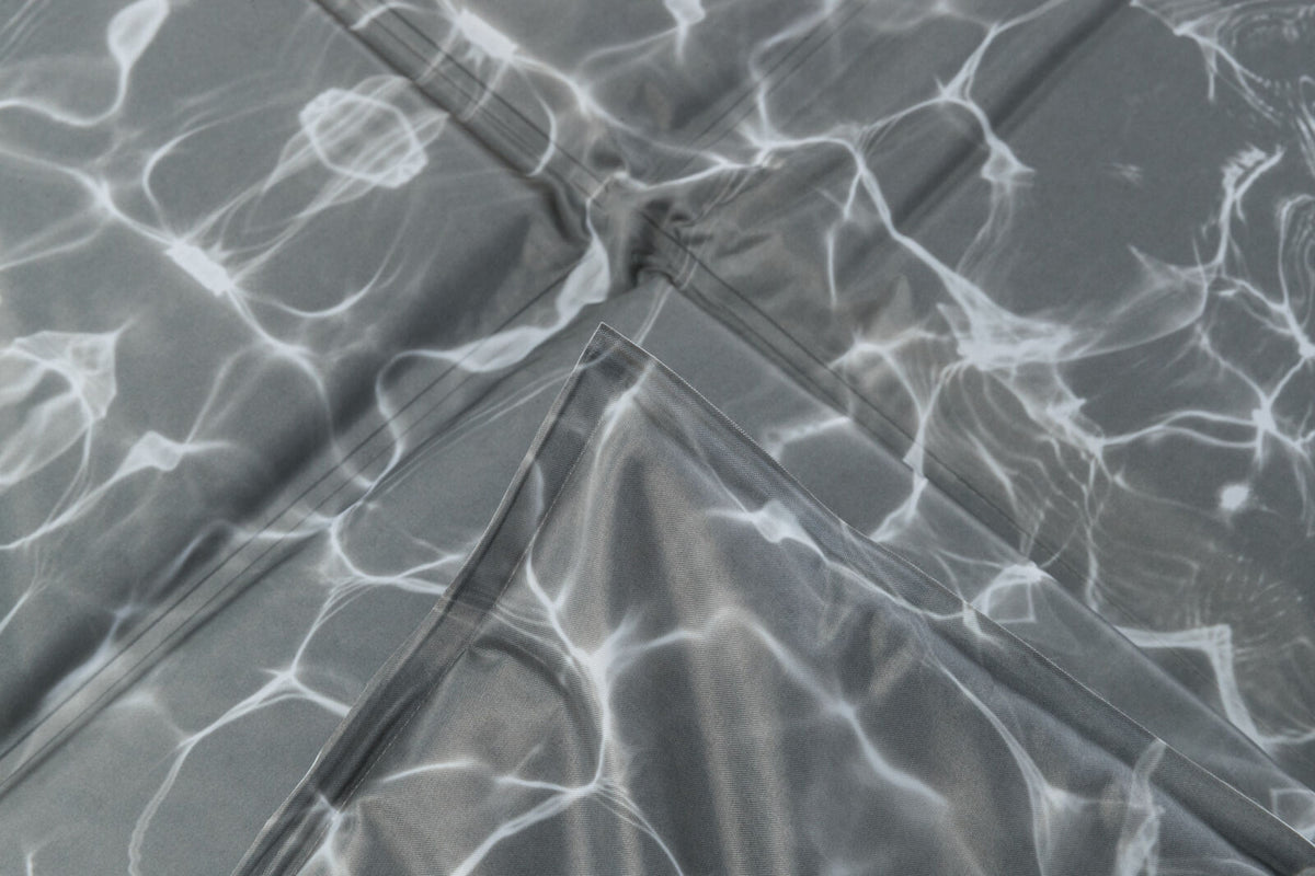 Graues gefaltetes Material mit weißen, fließenden Linien, die an Lichtreflexionen auf Wasser erinnern.