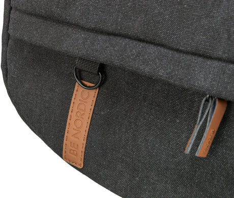 Grauer Stoff mit braunem Lederetikett beschriftet "BE NORDIC", schwarzer Metallring und zwei Lederriemen sichtbar.