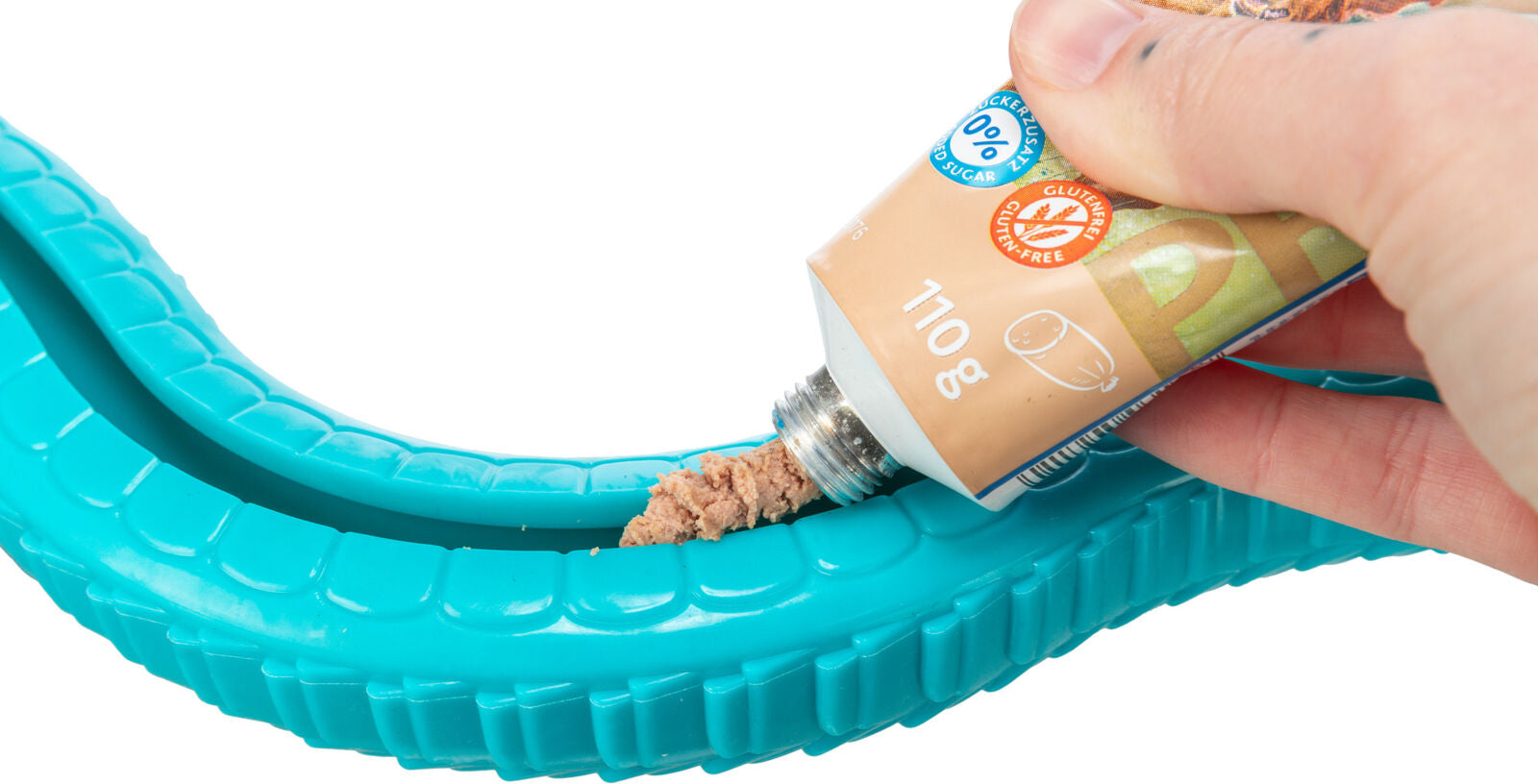 Eine Hand drückt Fleischpaste aus einer beige Tube in eine blaue, wellenförmige Kunststoffvorrichtung.