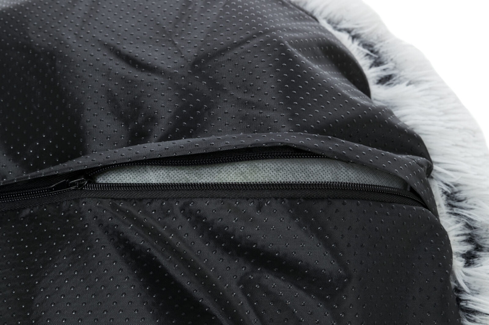 Nahaufnahme eines schwarzen, gepunkteten Stoffes mit einem halb geöffneten Reißverschluss und weißem, fellartigem Rand.