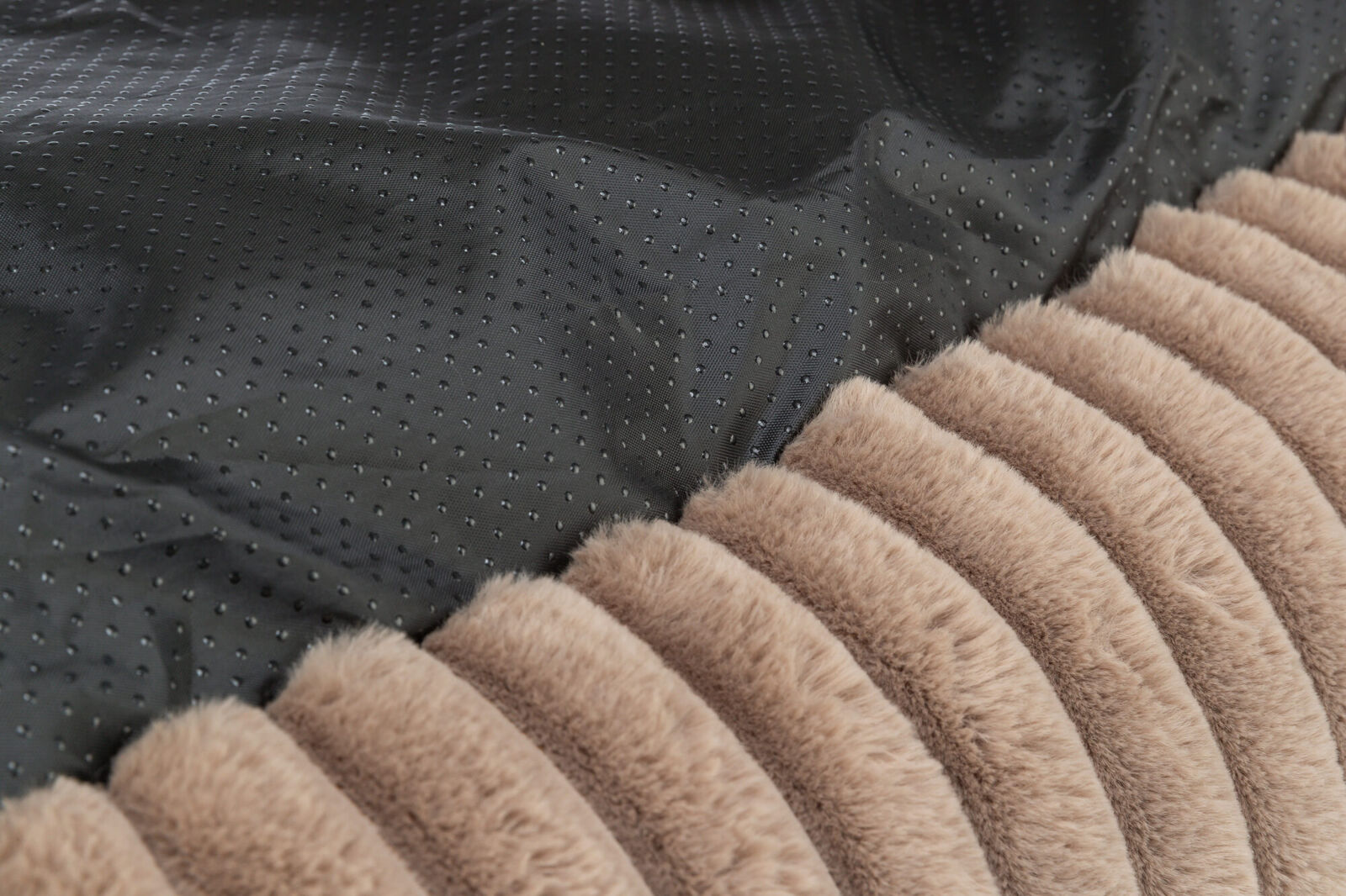 Schwarzer, gepunkteter Stoff neben einem gestreiften, beige-braunem Pelzmaterial in Nahaufnahme.