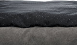 Die Aufnahme zeigt einen Stoff mit einer grauen, gewebten Textur und darüberliegendem schwarzen, gepunkteten Material.