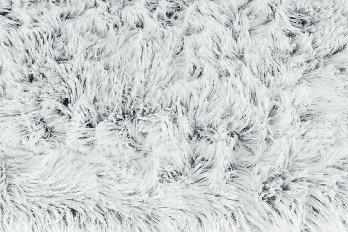 Flauschige, weiße Oberfläche mit dichtem, langem Flor aus weichem Material in unregelmäßigen Mustern.