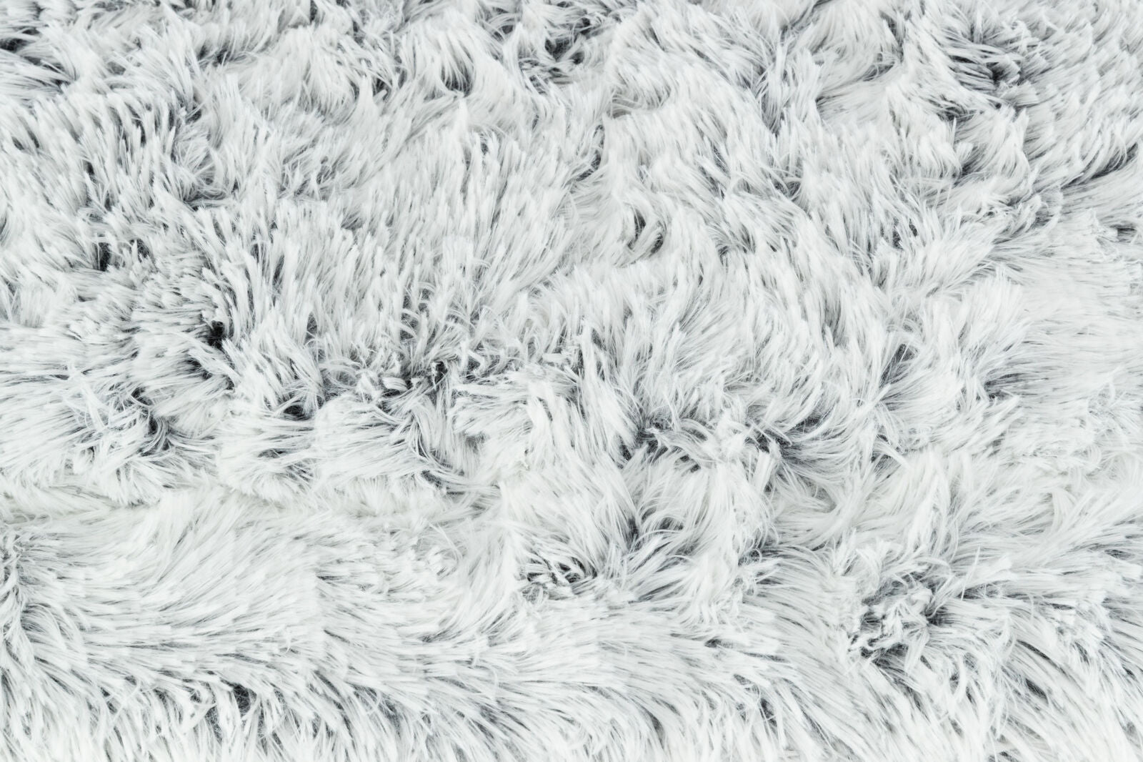Flauschige, weiße Oberfläche mit dichtem, langem Flor aus weichem Material in unregelmäßigen Mustern.