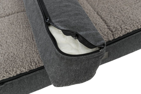 Graues Hundebett mit abnehmbarem Bezug, offenen Reisverschluss zeigend, und flauschiger, beige-weißer Oberfläche.