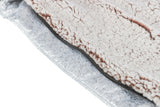 Flauschiger Stoff in Cremefarbe mit einem Reißverschluss auf einer metallischen, silbrigen Oberfläche.