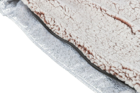 Flauschiger Stoff in Cremefarbe mit einem Reißverschluss auf einer metallischen, silbrigen Oberfläche.