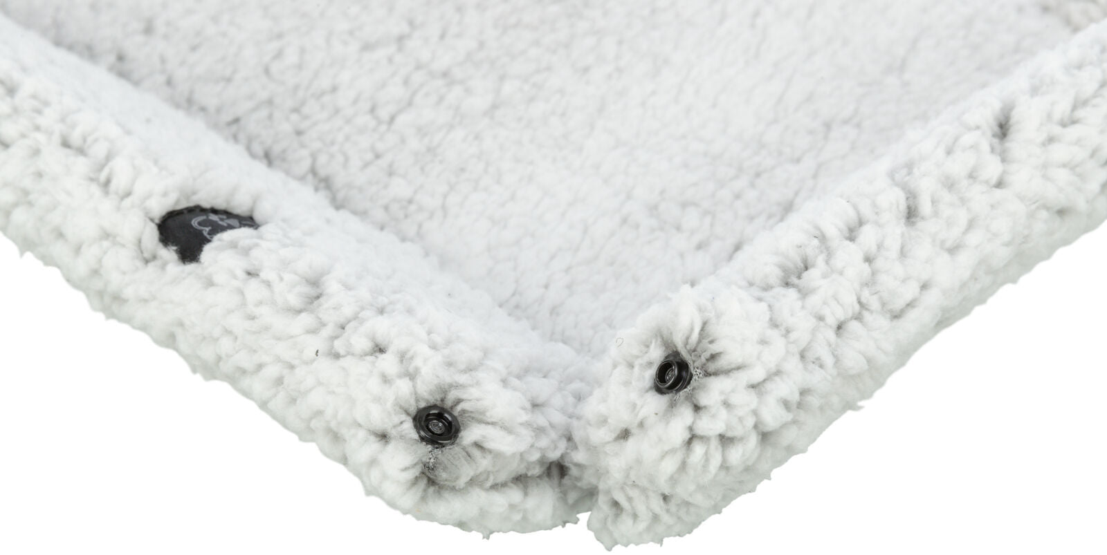 Eine weiße, flauschige Decke mit einer dichten Textur, schwarzen Knöpfen und einem kleinen, schwarzen Etikett.