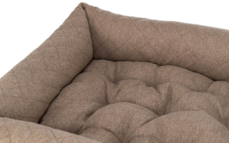 Beiges, gesteppte Kissen mit weicher, gepolsterter Oberfläche in einer Ecke angeordnet.