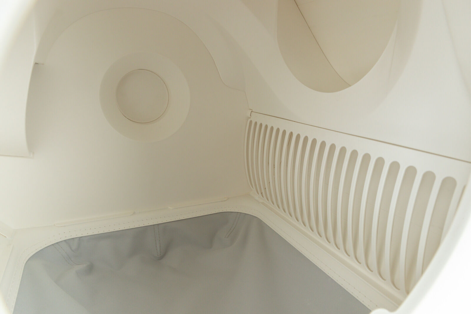 Innenansicht einer hellen, glattwandigen Struktur mit kreisförmigen und gerillten Elementen, darunter ein grauer Einsatz.