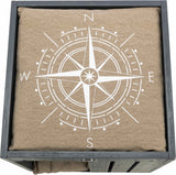 Kompassdesign in Weiß auf beigem Stoff in einer grauen Holzkiste, Himmelsrichtungen N, E, S, W markiert.