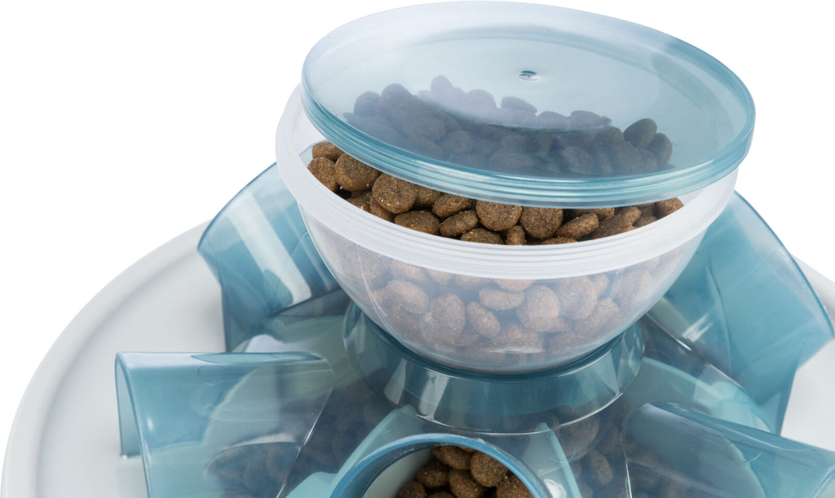Transparenter Futterspender mit blauem Deckel, gefüllt mit braunen Trockenfutter-Pellets auf weißem Untergrund.