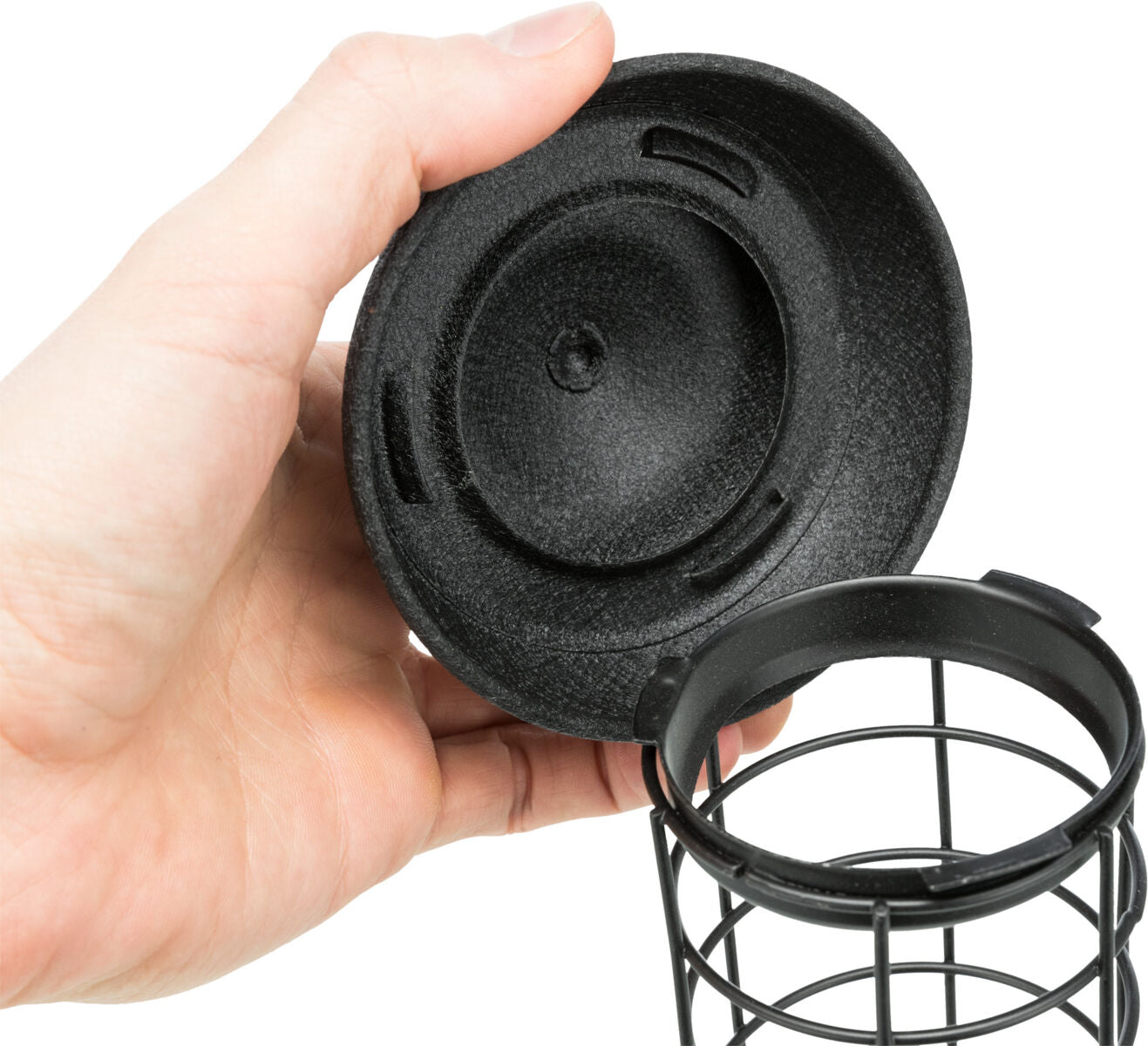 Hand hält schwarzen Kunststoffdeckel und Gitterkorb aus Metall, Detailaufnahme.