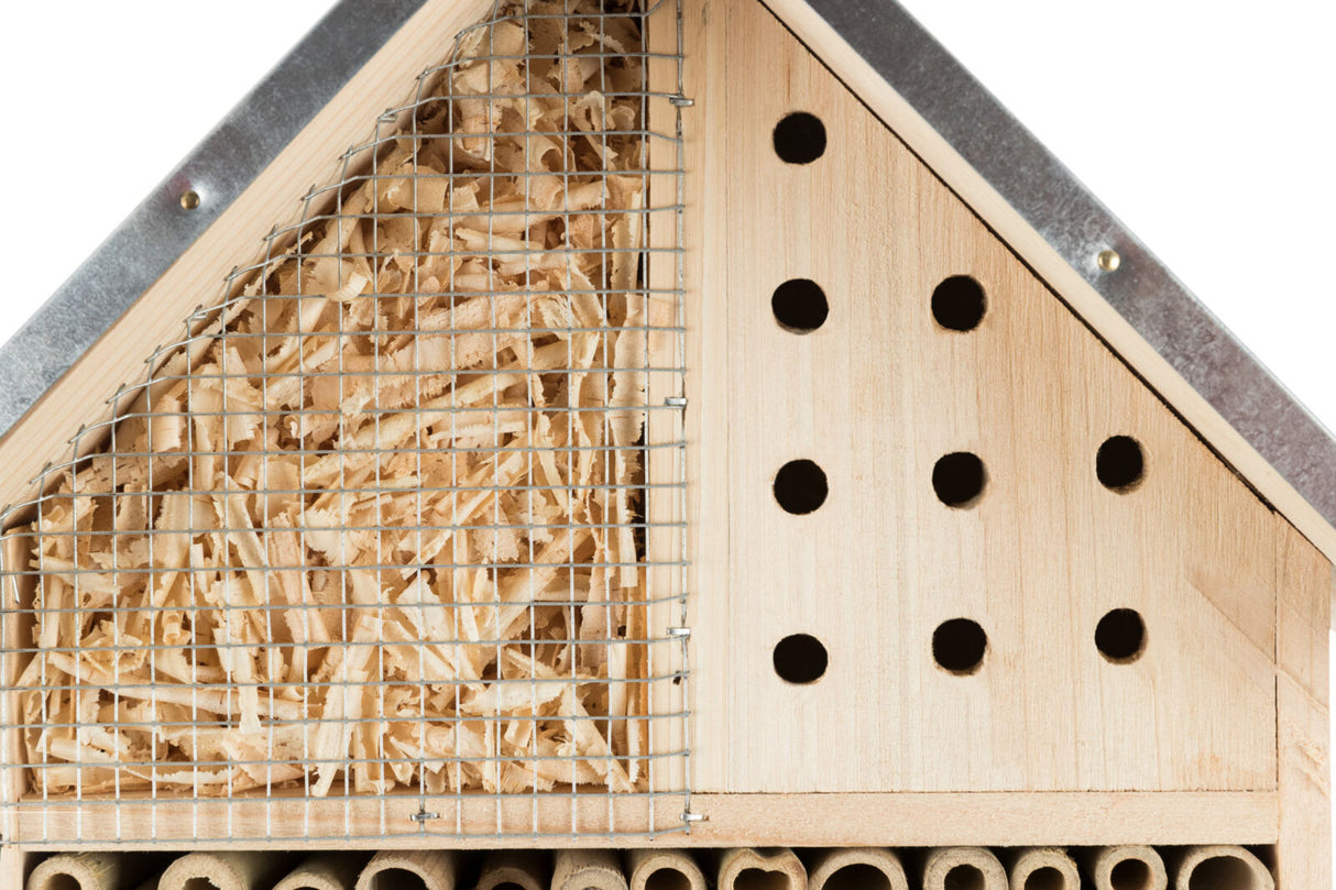 Holz-Insektenhotel mit Gitter, gefüllt mit Holzspänen, daneben perforiertes Holzbrett, unten Röhren.