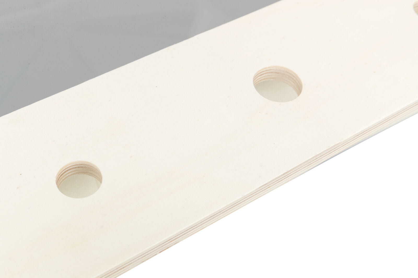 Helles Holzbrett mit drei runden Löchern auf einer Seite und grauer Fläche im Hintergrund.