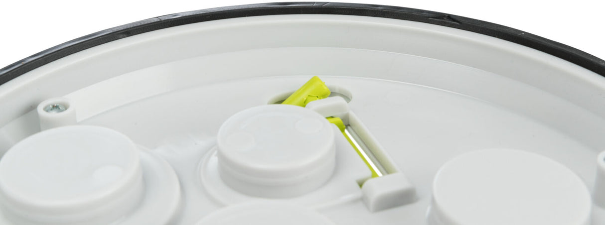 Runder weißer Plastikdeckel mit schwarzem Rand, sichtbare Schraube und grünes Element im Inneren.