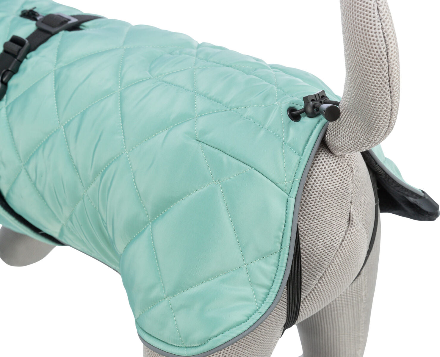 Ein mintgrüner, gesteppter Hundemantel mit schwarzem Verschluss und elastischem Band auf einem grauen Stoffmodell.