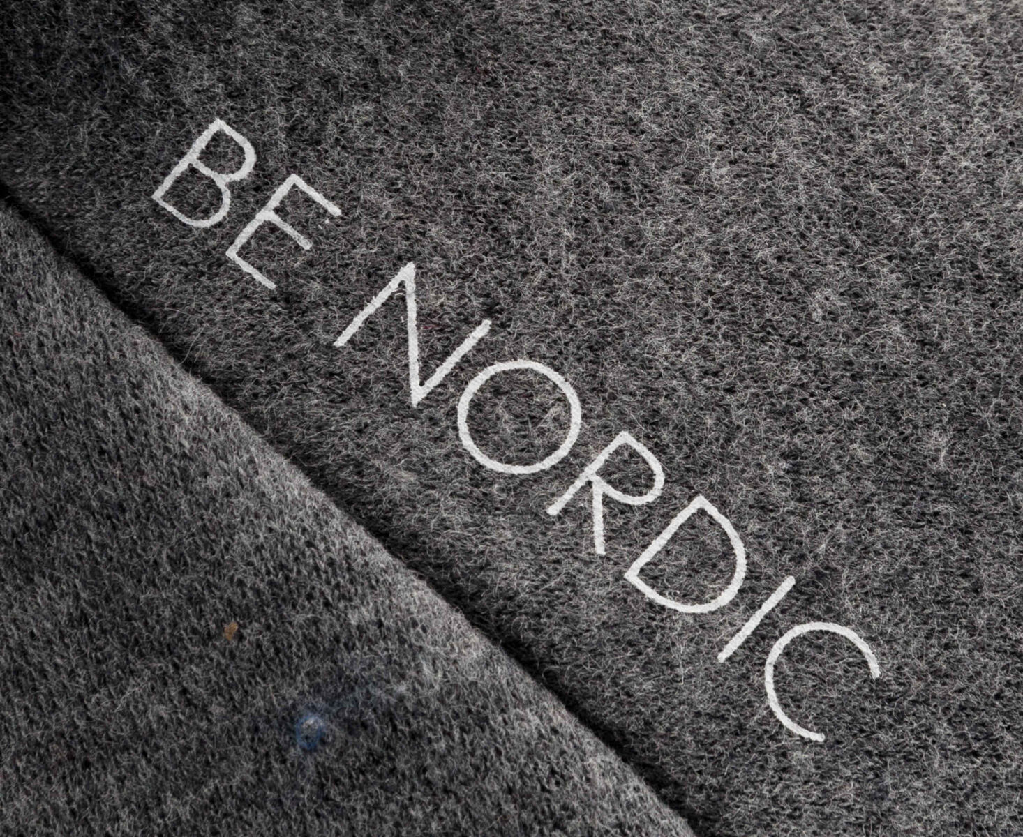 Grauer Textilstoff mit der Aufschrift "BE NORDIC" in weißen Buchstaben.
