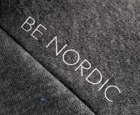 Grauer Textilstoff mit der Aufschrift "BE NORDIC" in weißen Buchstaben.