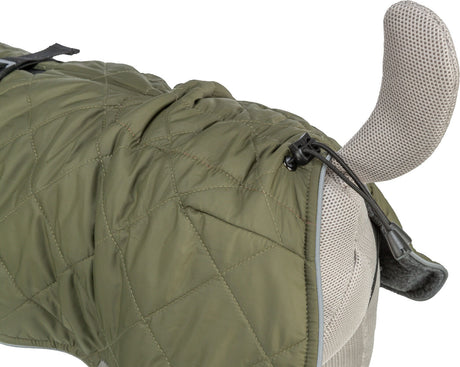 Grüne gesteppte Hundejacke mit verstellbaren Verschlüssen auf einem grauen Stoffmodell, sichtbar von der Seite.