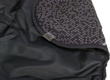 Schwarzer Stoff mit geometrischem Muster in Lila und Grau, Label mit "TRIXIE"-Schriftzug sichtbar.