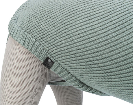 Gestricktes, hellgrünes Textil auf einem beige-farbenen, texturierten Hintergrund mit einem kleinen schwarzen Etikett.