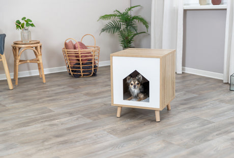 Holzfarbene Höhle mit weißer Front in Wohnzimmer, Hund sitzt darin, Laminateboden, Pflanzen im Hintergrund.