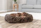 Hund liegt in braunem Bett mit Leopardenmuster auf Holzfußboden im Wohnzimmer.