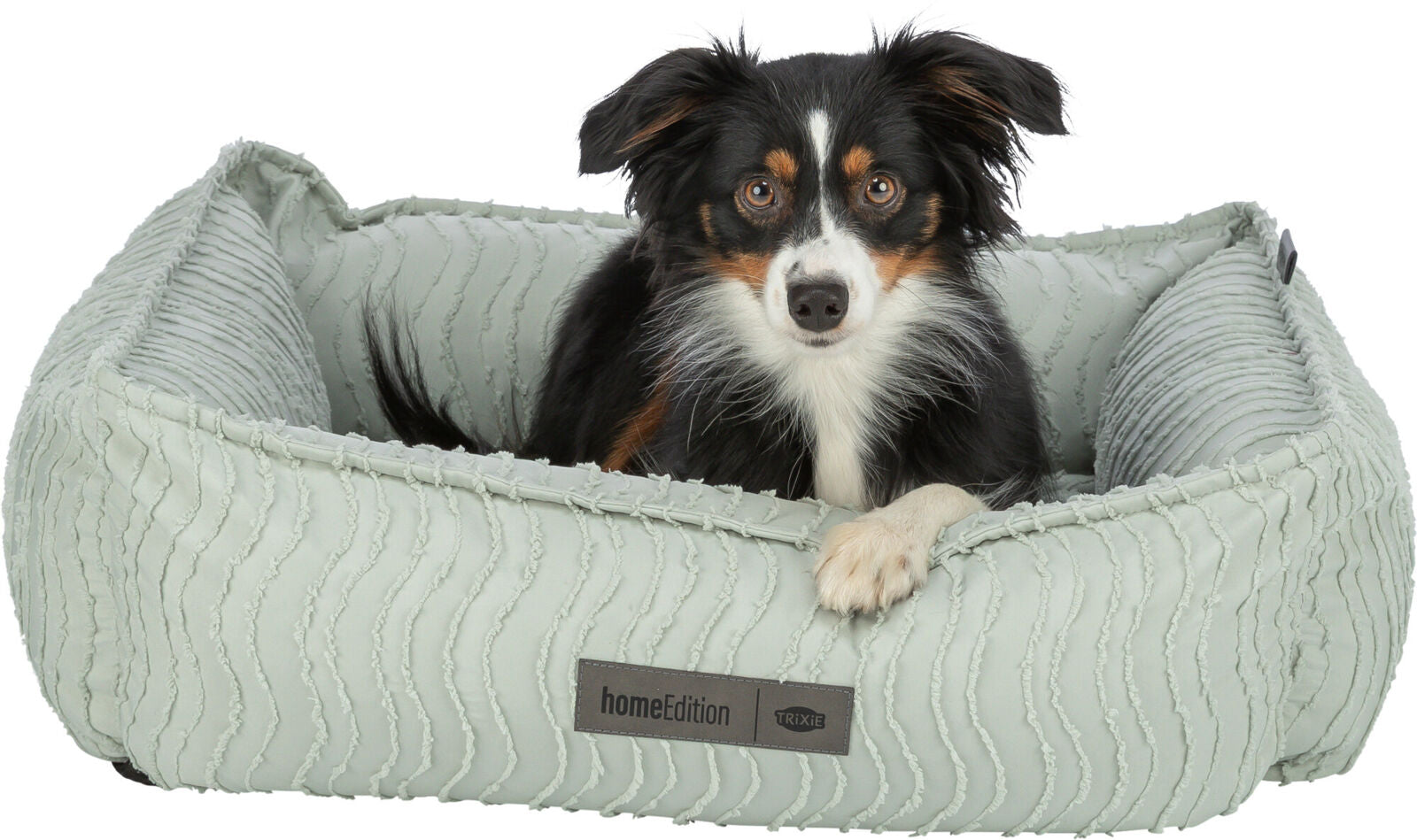 Hund liegt in einem hellen, gerippten Hundebett mit „homeEdition TRIXIE“-Etikett.
