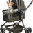 Ein kleiner Hund sitzt in einem grün-schwarzen Kinderwagen mit einem Netz und braunem Griff.