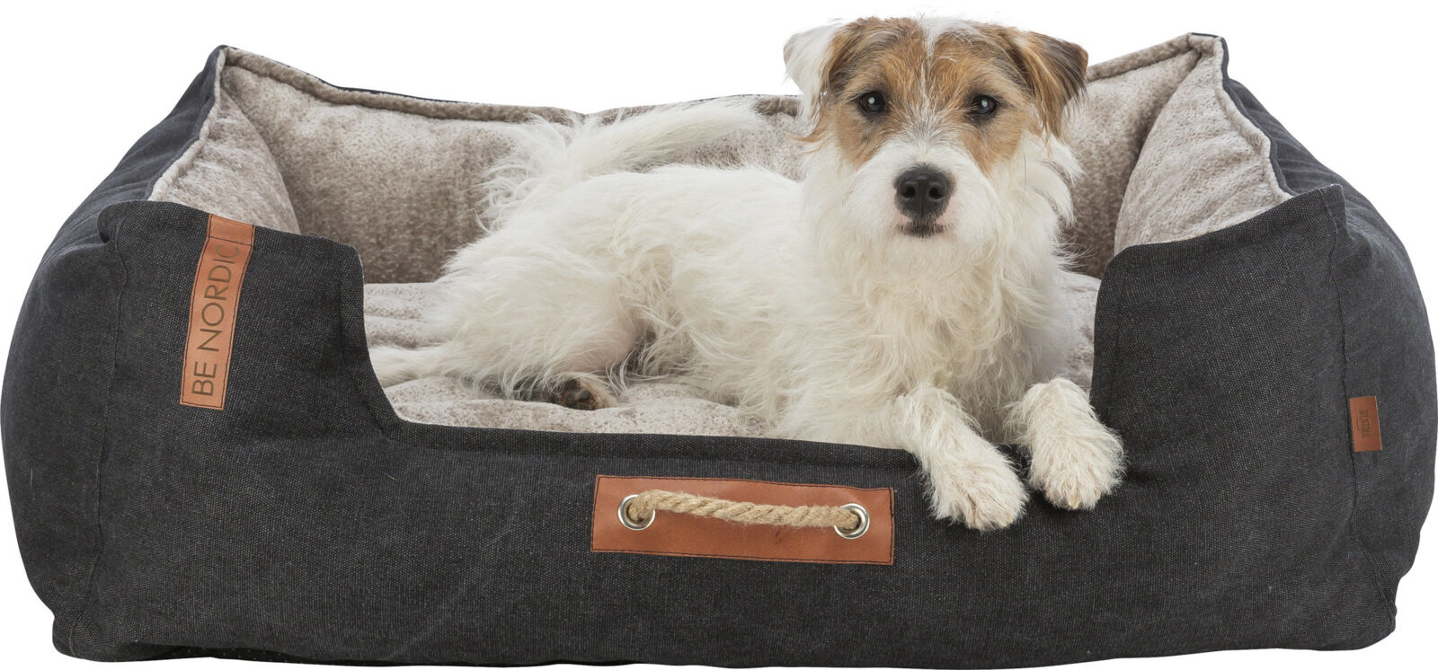 Ein Hund liegt in einem grauen Hundebett mit beigem Innenfutter, darauf ein Lederetikett mit Aufschrift "BE NORDIC".