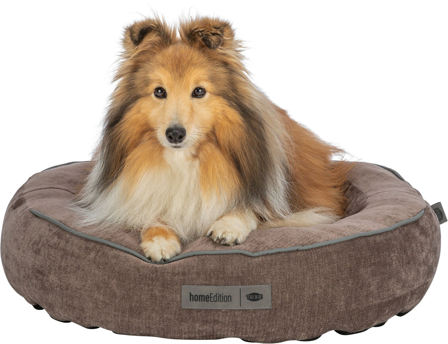 Brauner Hund sitzt auf einem runden, braunen Hunde-Bett mit weichem Rand und Etikett "homeEdition".