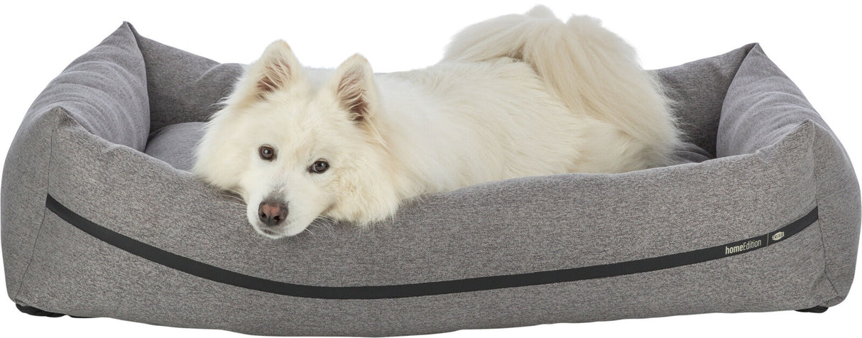 Weißer Hund liegt in einem grauen Hundebett mit schwarzen Streifen und dem Logo "homeEdition".