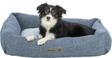 Ein schwarz-weißer Hund liegt in einem blauen Hundebett mit einem Kissen und einem Etikett mit der Aufschrift "homeEdition".