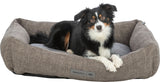 Ein Hund liegt in einem grauen Hundebett mit einem Etikett, auf dem "homeEdition TRIXIE" steht.