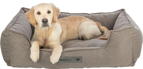 Heller Hund liegt in einem braunen Hundebett aus Stoff, auf dem Etikett steht "homeEdition" und "TRIXIE".